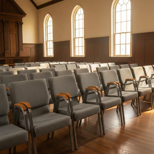 Rows of gray chairs with wooden armrests in a church setting with large windows.
